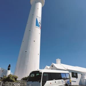 Kleiner Reisebus vor hohem, weißen Leuchtturm