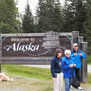 Drei Touristen vor einem Willkommen in Alaska Schild